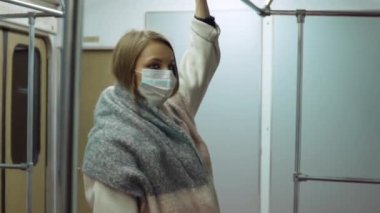 Tıbbi maskeli bir kız metro vagonunda duruyor.