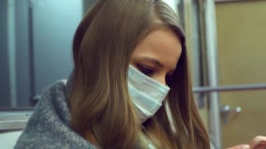 Tıbbi maskeli bir kız metro vagonunda oturuyor ve ekranı parçalıyor.