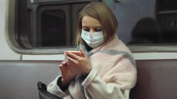 Mädchen mit medizinischer Maske sitzt in einem U-Bahn-Wagen und scrooll screen — Stockvideo