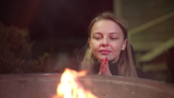 En vit flicka värmer upp nära elden. — Stockvideo
