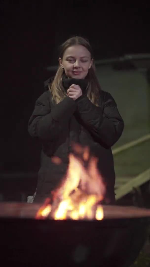 Uma menina caucasiana aquece perto do fogo — Vídeo de Stock