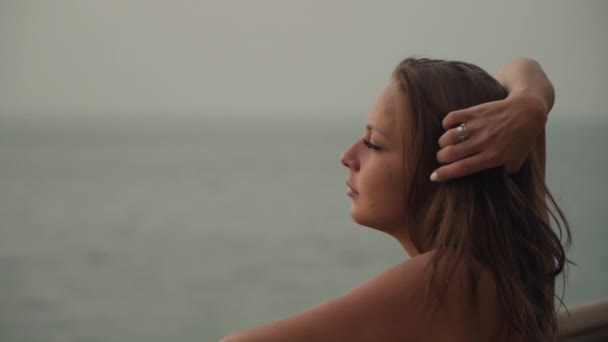 Hermosa chica caucásica alisando su cabello contra un fondo de puesta de sol — Vídeo de stock
