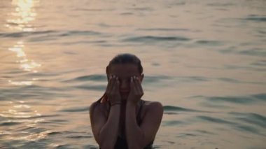 girl bathes in the sea against the backdrop of the sunset