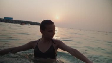 girl bathes in the sea against the backdrop of the sunset