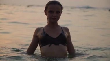 woman in a swimsuit smiles and swims in the ocean in the evening