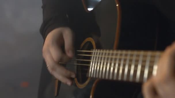 Ένας άντρας με μαύρη μπλούζα παίζει ακουστική κιθάρα. — Αρχείο Βίντεο