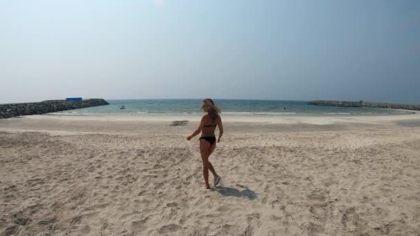 Дівчина в чорному купальнику біжить уздовж пляжу — стокове відео