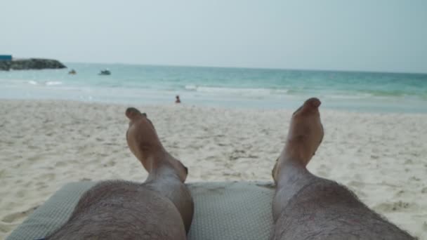 Mans benen op een zandstrand. Hij ligt te zonnebaden aan de kust. — Stockvideo