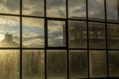 Terk edilmiş fabrikanın kirli penceresinden içeri güneş giriyor.
