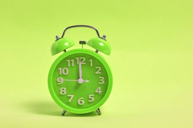 Parlak yeşil bir arkaplanda çalar saat yeşil. Öğle yemeği vakti, saat 12.