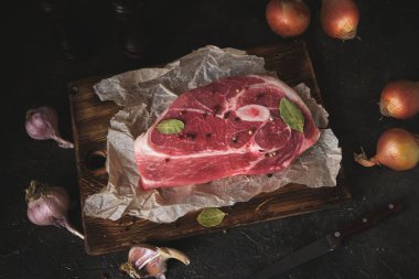 Eski bir kesme tahtasında çiğ domuz eti, bıçak, baharat ve malzemeler yan yana konur.