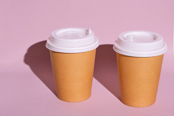 Disposable cups for hot coffee or tea on a pink background in the bright sun