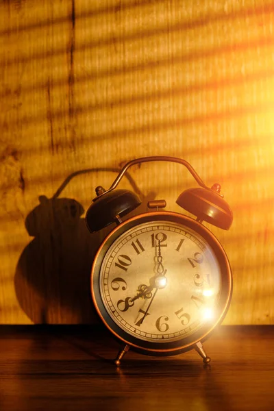 旧时的闹钟在清晨的桌上 背景上是窗帘的阴影 — 图库照片