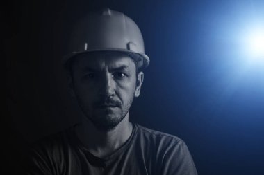 Miğferli bir madenci ve kirli yüzlü bir atlet. Arkaplanda parlak mavi ışık.