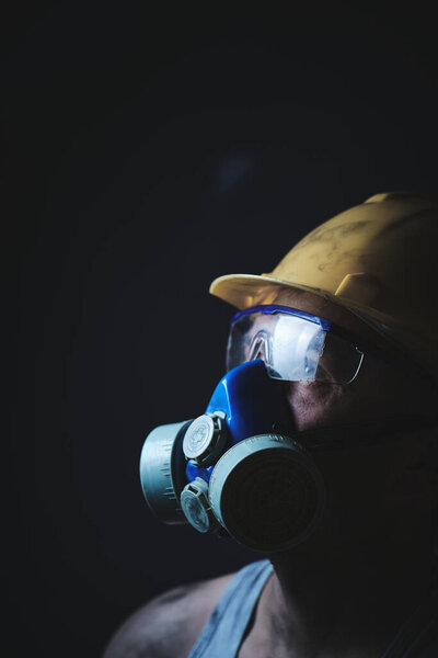 Profile portrait miner in helmet, respirator and goggles, looking at light.Dirty worker in shirt