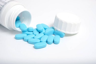 Beyaz arka planda şişeden mavi haplar saçılıyor.