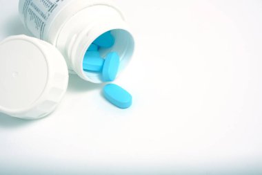 Beyaz arka planda şişeden mavi haplar saçılıyor.