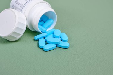 Yeşil arka planda şişeden mavi haplar saçılıyor.