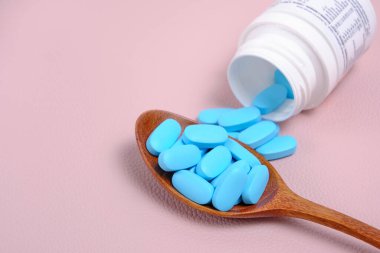 Pills, vitamins in wooden spoon, poured out of a bottle, on a pink background