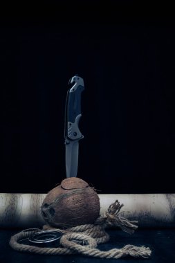 Taktik katlama bıçağı, ipin yanında duran bölünmüş hindistan cevizine ve karanlık arka planda eski bir haritaya sıkışmış.