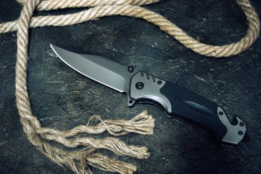 Taktik bıçak ve kayalık arka planda ip kesme. Hayatta kalma ve macera.