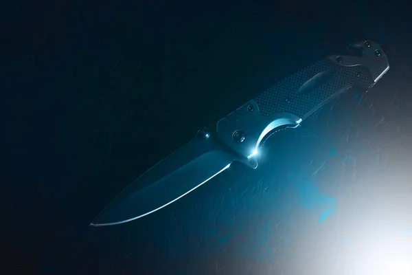 深色背景下的战术折叠刀被明亮的蓝光照亮 — 图库照片