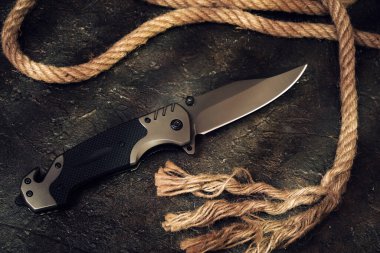 Taktik bıçak ve kayalık arka planda ip kesme. Hayatta kalma ve macera.