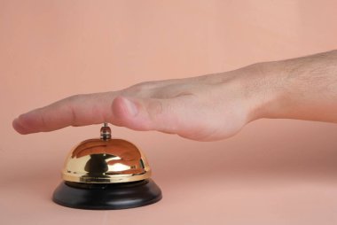 Pastel bej arka plan üzerinde eliniz ile otel servisi çağrı düğmesine basmak. Kavramsal otel, seyahat ve dinlenme