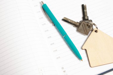 Anahtarlı anahtarlık şekilli ev ve açık bir defter üzerinde tükenmez kalem.