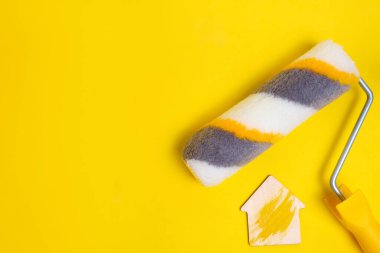 Sarı arka planda duvarları boyamak için boya silindiri ve bir ev figürü. Ev yenileme kavramı.