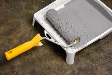 Tablada sarı saplı boya silindiri var. Beton zeminde gri boya var.