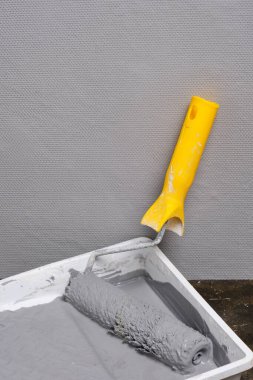 Sarı saplı boya silindiri gri duvarlı arka planda gri boyalı rulo için.
