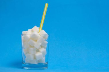 Rafine şeker küplü bir bardak ve mavi arka planda bir içme tüpü.