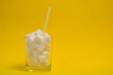 Rafine şeker küplü bir bardak ve sarı arka planda bir içme tüpü.