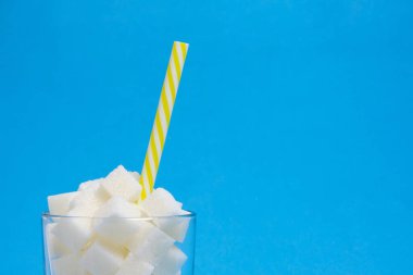 Rafine şeker küplü bir bardak ve mavi arka planda bir içme tüpü.