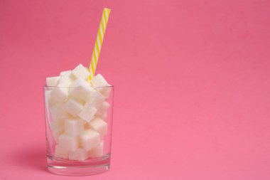 Rafine şeker küplü bir bardak ve pembe arka planda bir içecek tüpü.