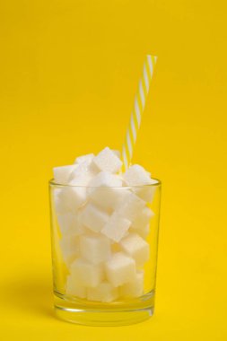 Rafine şeker küplü bir bardak ve sarı arka planda bir içme tüpü.