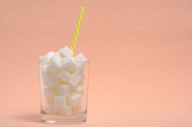 Rafine şeker küpleri ve bej arka planda bir içme tüpü olan bir bardak.