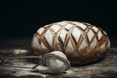 Üzerine un serpiştirilmiş çavdar ekmeği ve koyu arkaplana serpiştirmek için elek.