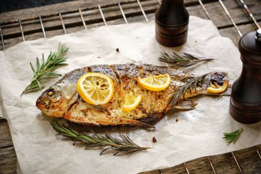Parşömen kağıdında pişmiş, baharatlı fırında balık, limon ve biberiye. Ahşap arka planda ızgara ızgara ızgara.
