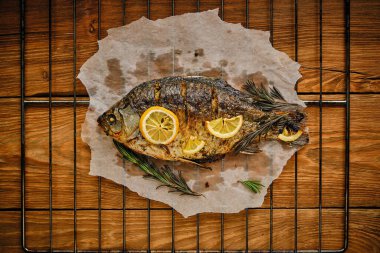 Baharatlı, limonlu, biberiyeli ve ahşap kaplama ızgaralı parşömen kağıdında pişmiş balık.