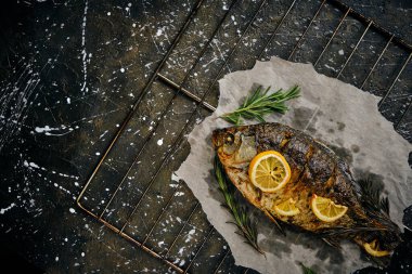 Fırında limon ve parşömen kağıdında biberiye ile pişirilmiş balık, ızgara üzerine serilmiş koyu arkaplan.