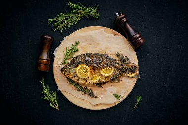 Limonlu ve biberiyeli fırında pişirilmiş balık kesme tahtası ve parşömen kağıdıydı. Koyu arkaplanda iki pipet vardı.