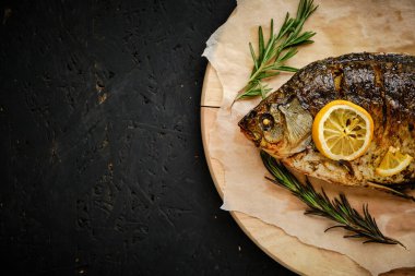 Limonlu ve biberiyeli fırında pişirilmiş balık kesme tahtası ve parşömen kağıdı. Koyu arkaplanda.