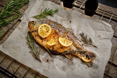 Parşömen kağıdında pişmiş, baharatlı fırında balık, limon ve biberiye. Ahşap arka planda ızgara ızgara ızgara.