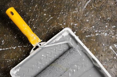 Tablada sarı saplı boya silindiri var. Beton zeminde gri boya var.