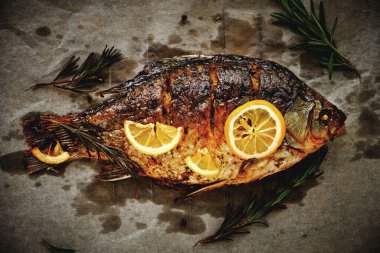 Parşömen kağıdında pişmiş, baharatlı fırında balık, limon ve biberiye.