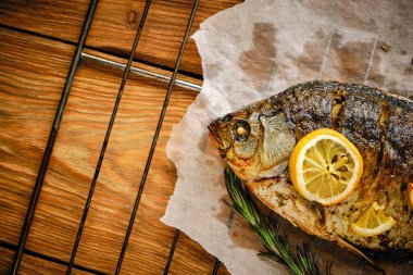 Baharatlı, limonlu, biberiyeli ve ahşap kaplama ızgaralı parşömen kağıdında pişmiş balık.