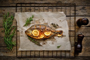 Parşömen kağıdında pişmiş, baharatlı fırında balık, limon ve biberiye. Ahşap arka planda ızgara ızgara ızgara.