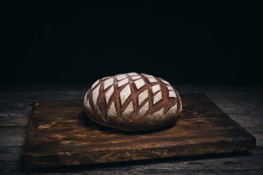 Kırsal ahşap arka planda un serpiştirilmiş somun siyah çavdar ekmeği.